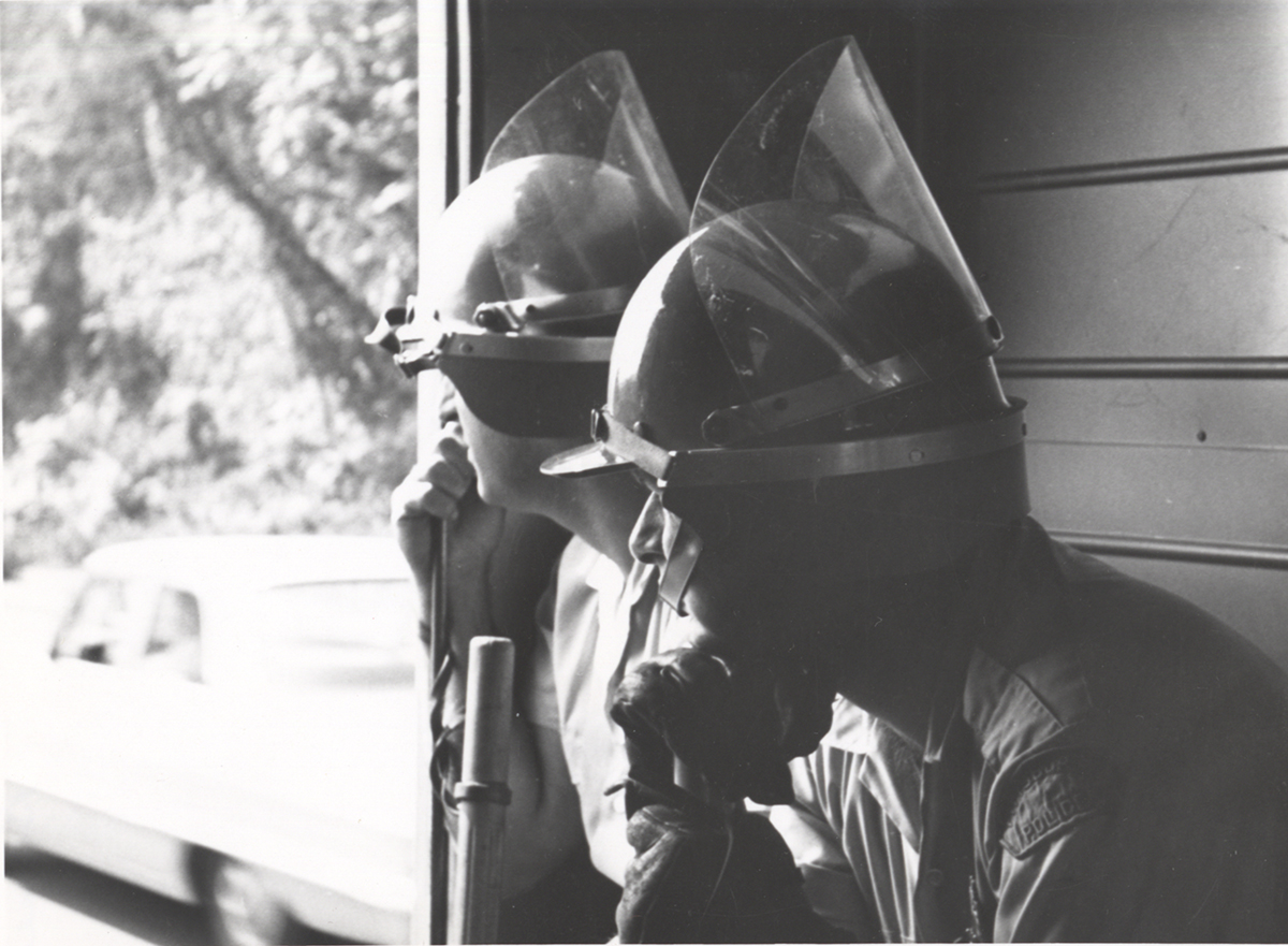 Two unidentified policemen don riot helmets with attached face shields from the 1960s.