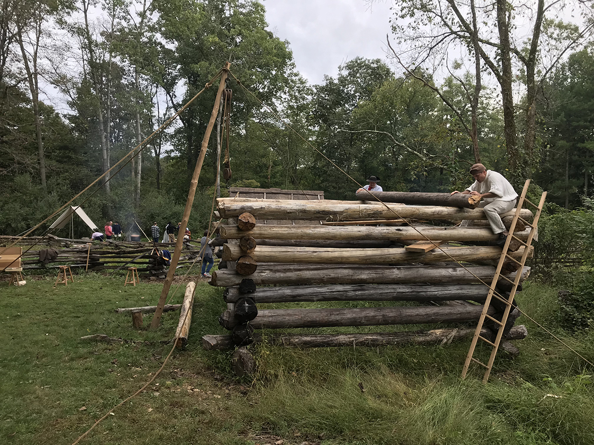 Two carpenters marking the notches for the next log to be put onto the Meadowcroft cabin.