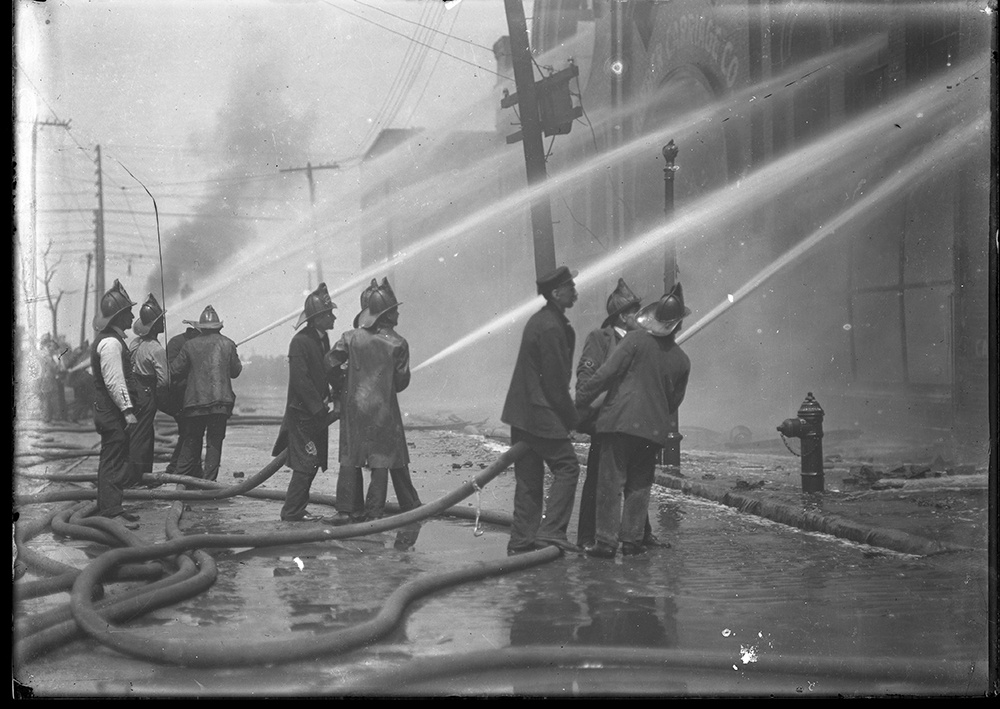 A group of firemen using hoses to put out a fire at the Gerber Carriage Co. in downtown Pittsburgh, 1904.