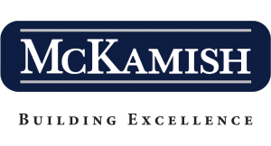 McKamish logo with “McKamish” in bold white capital letters on a dark blue rectangular background; below, the tagline “BUILDING EXCELLENCE” appears in smaller black capital letters.