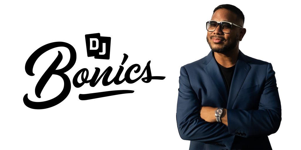 A man in a blue suit with glasses stands with his arms crossed, smiling slightly. Next to him, bold black script text reads DJ Bonics on a white background. The image celebrates his role at History Uncorked.