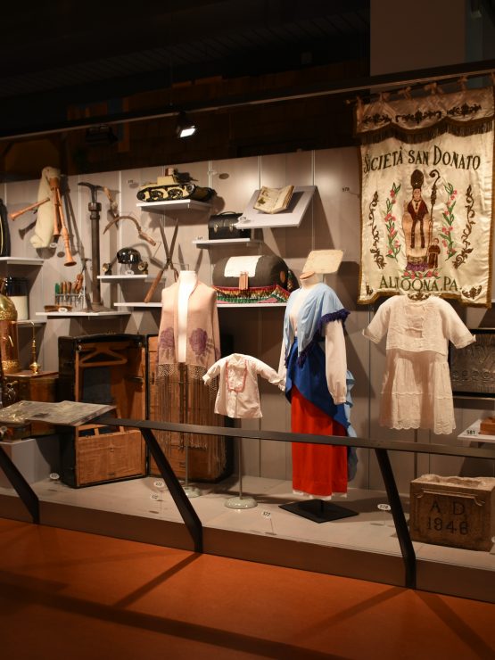 A museum exhibit shows religious artifacts, statues, crosses, banners, and historic items on display behind glass with focused lighting. *AI generated alt text