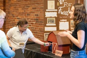 A woman gestures to a small barn model with an