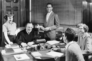 Black-and-white photo of a judge at his desk with four young adults holding act 48 papers in an office lined with books and papers. *AI generated alt text