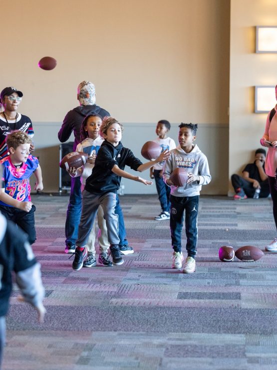 Children and adults take part in an indoor football throwing activity, aiming at a target, with a man in athletic wear in front. *AI generated alt text