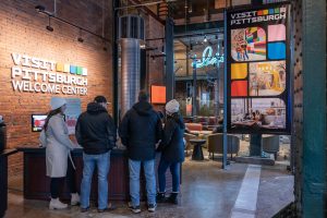 A group of visitors stands at the counter inside the museum, with signs and historic photos in the background, exposed brick walls visible. *AI generated alt text