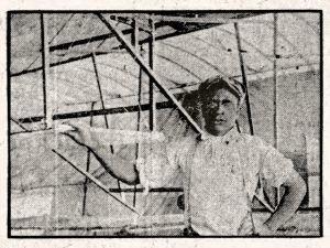 Black and white image of a young man in a cap and light shirt, resting his hand on an early aircraft or glider's wooden frame. *AI generated alt text