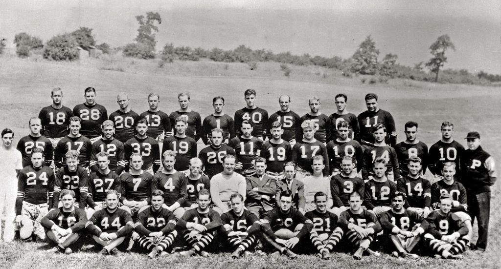 Black-and-white photo of a vintage American football team, over 40 players and coaches, outdoors in numbered jerseys and striped socks. *AI generated alt text