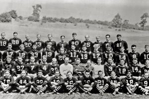 Black-and-white photo of a vintage American football team, over 40 players and coaches, outdoors in numbered jerseys and striped socks. *AI generated alt text
