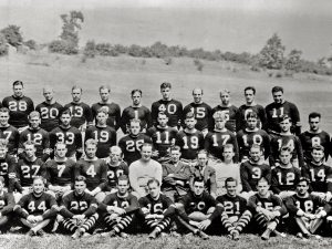 Black-and-white photo of a vintage American football team, over 40 players and coaches, outdoors in numbered jerseys and striped socks. *AI generated alt text