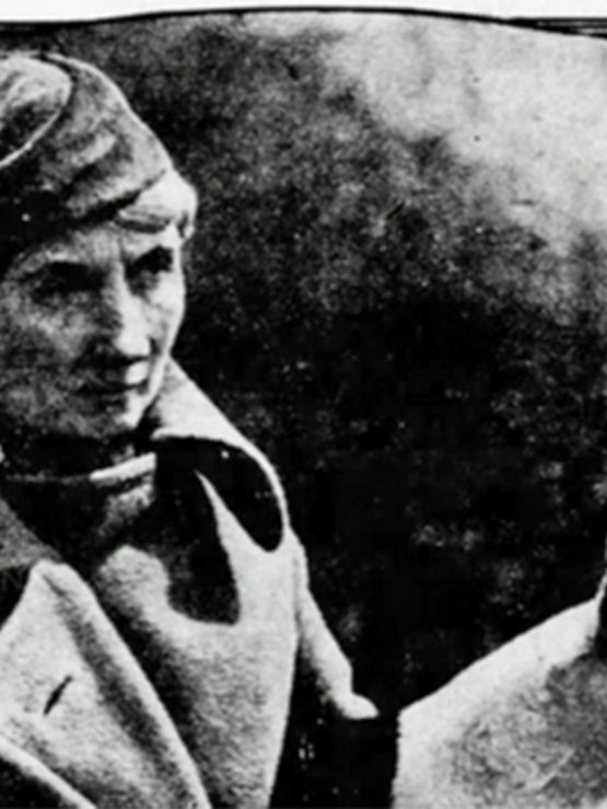 Black and white vintage photo of a person in a cap and coat standing beside a pointed-eared dog, with blurred background. *AI generated alt text