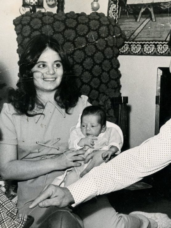 A young boy kicks a football indoors as a woman with a baby and a man sit nearby. A decorated Christmas tree stands in the background. *AI generated alt text