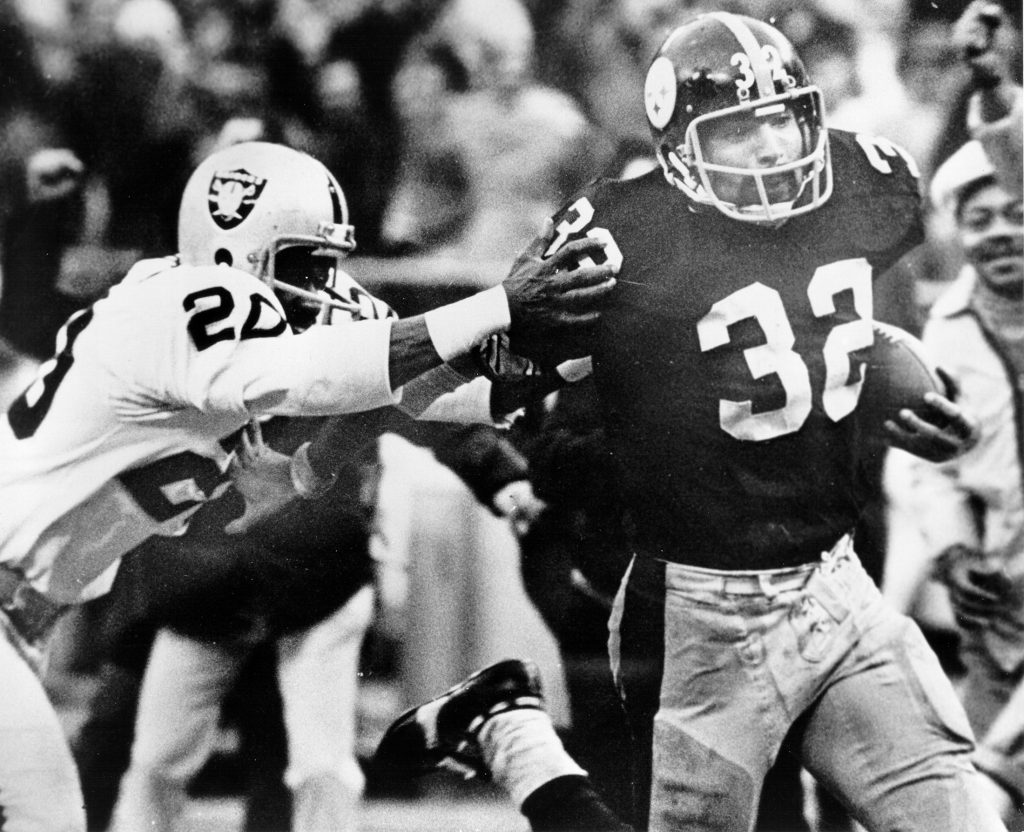 A football player wearing number 32 runs with the ball, fending off number 20, as a crowd observes the game in the background. *AI generated alt text