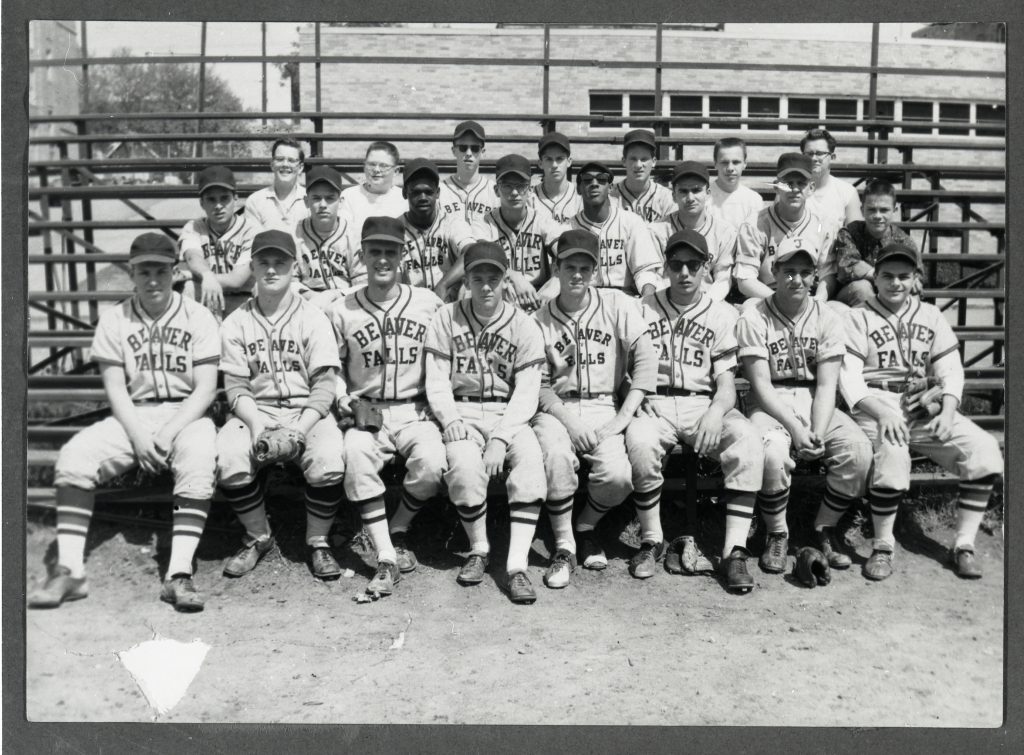 Black-and-white photo of Beaver Falls youth baseball team in uniform, about twenty boys and two adults posing on outdoor bleachers. *AI generated alt text