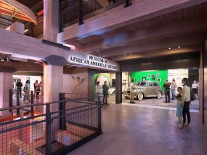 A museum interior with visitors viewing exhibits, a “Museum of African American History” sign, and a vintage car near a green wall. *AI generated alt text