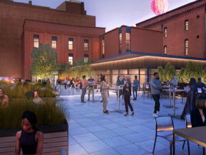 People gather on a modern rooftop terrace at dusk, sitting or standing near tables, with city buildings and greenery in the background. *AI generated alt text