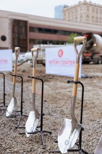 Three ceremonial shovels stand upright on a gravel lot with a HISTORY CENTER sign and construction equipment in the background. *AI generated alt text