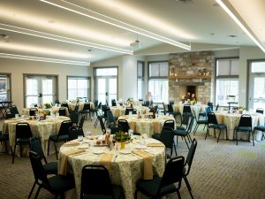 A historic banquet hall in the museum with round tables, patterned cloths, beige napkins, stone fireplace, and large windows. *AI generated alt text