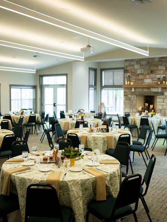 A historic banquet hall in the museum with round tables, patterned cloths, beige napkins, stone fireplace, and large windows. *AI generated alt text