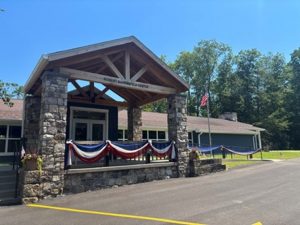 A stone museum with wooden roof and covered entrance, decorated in patriotic bunting, with an American flag and trees outside. *AI generated alt text