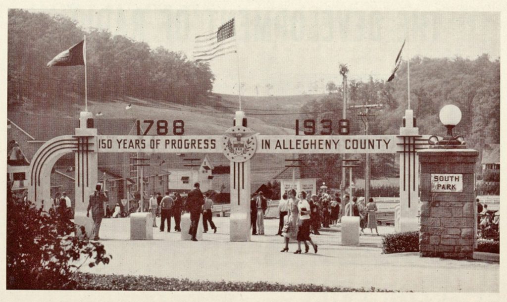 Black-and-white photograph showing a group of people gathered at the entrance to a park. An archway above the entrance displays the dates “1788 - 1938” and the phrase “150 Years of Progress in Allegheny County.” Flags are positioned around the archway, and a sign reads “South Park.” Trees and hills can be seen in the background. *AI generated alt text